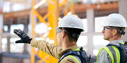 backview of two workers wearing hardhats and pointing at something
