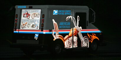 A U.S. Postal Service van has Scotchlite™ Reflective Graphic Film of a motorcycle that reflects light.
